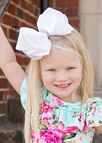 Young girl with a large white bow in her hair, wearing a floral dress.
