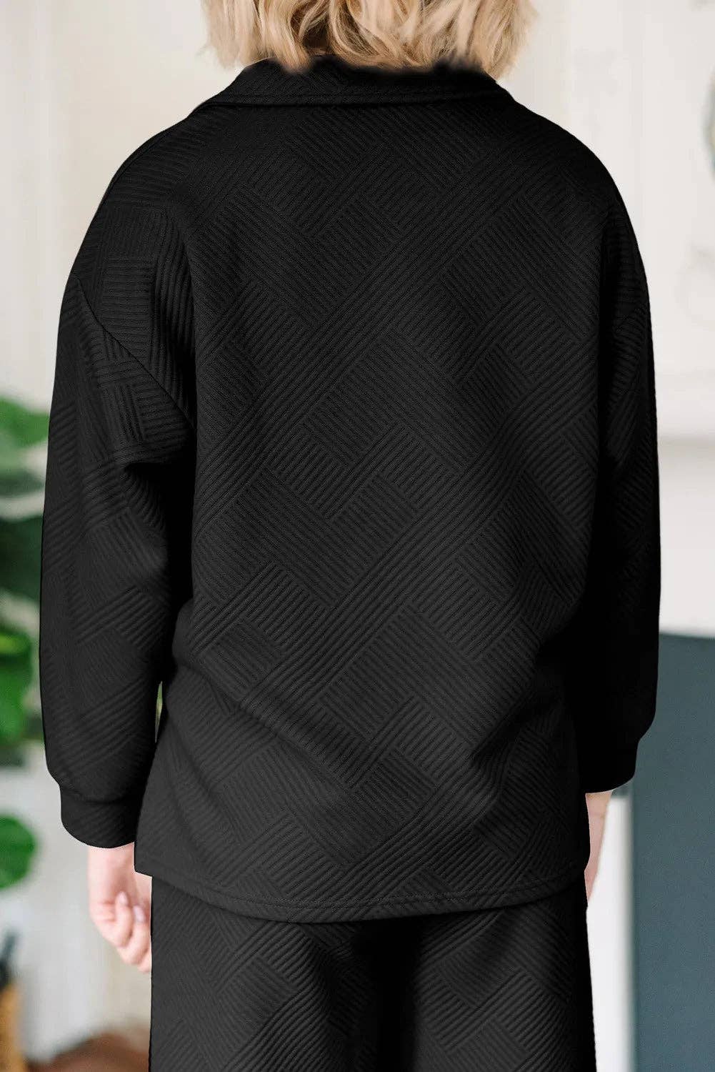 Person wearing a black textured jacket and pants in an indoor setting