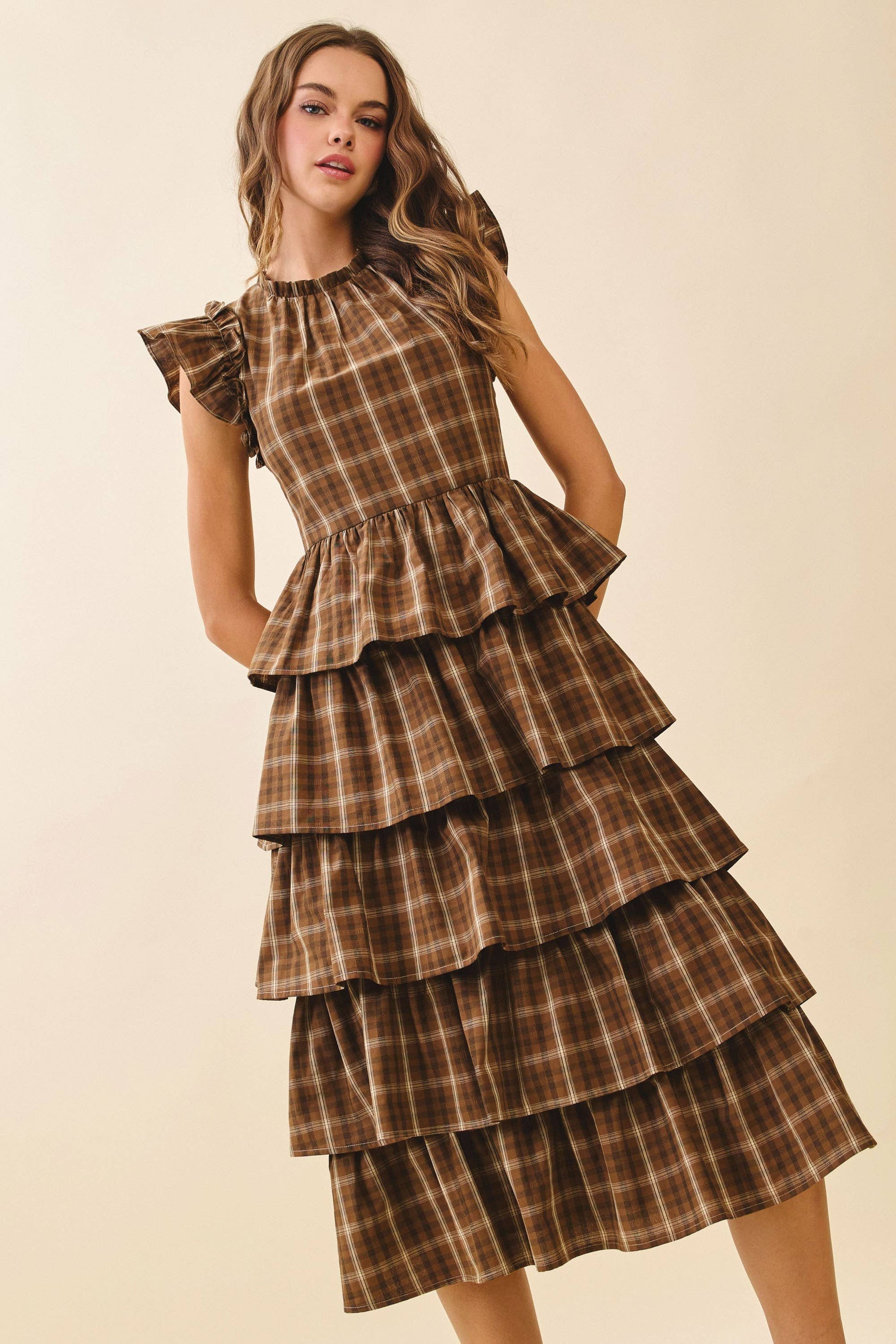 Woman wearing a brown plaid dress with ruffled layers on a beige background