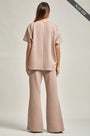 Woman wearing a beige outfit with wide-leg pants on a plain background