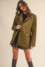 Woman wearing an olive green suede coat against a plain background