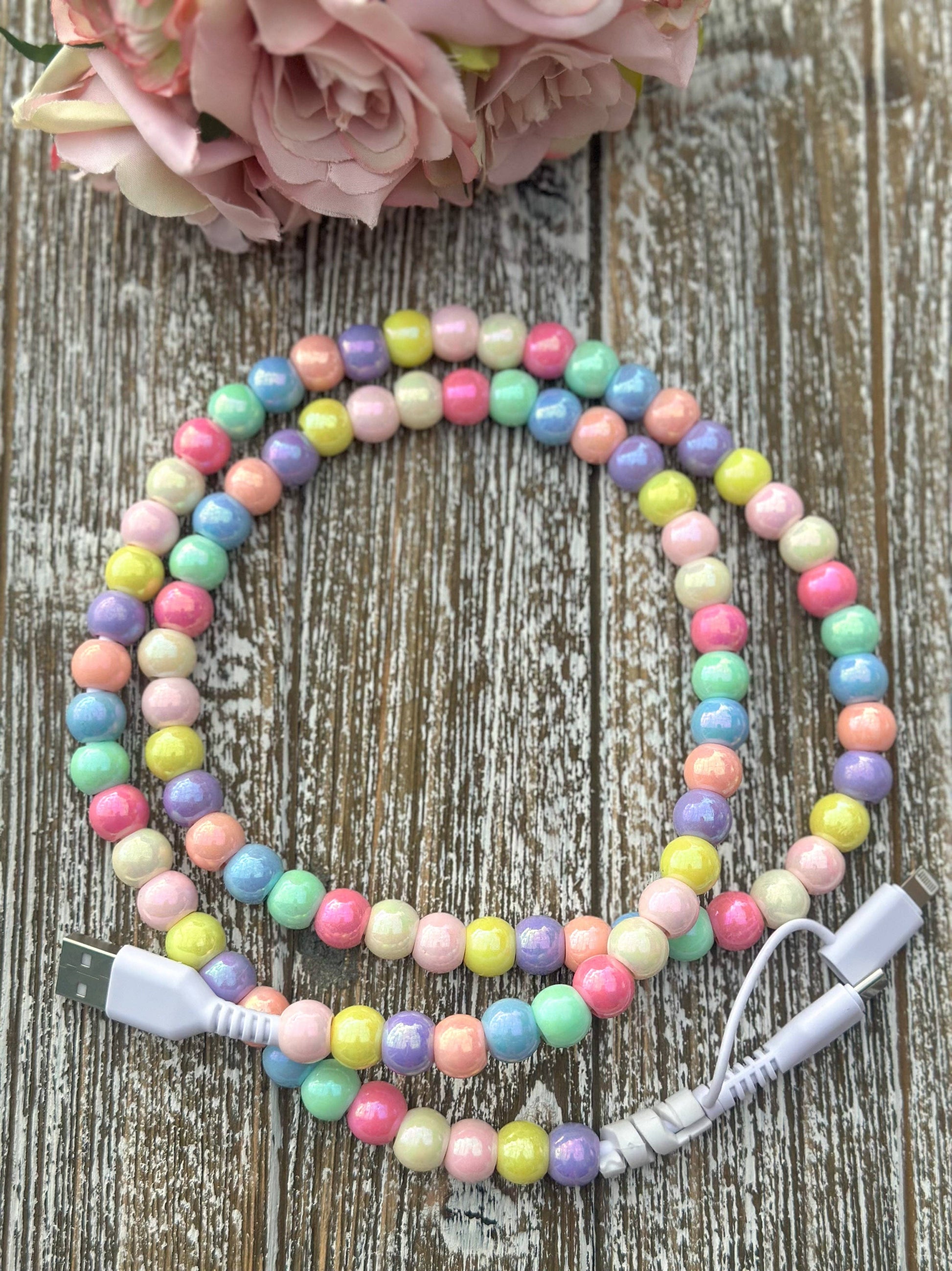 Colorful beaded USB cable on a wooden surface with pink flowers in the background