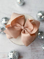 Large oatmeal colored  bow on a white surface with decorative silver balls in the background