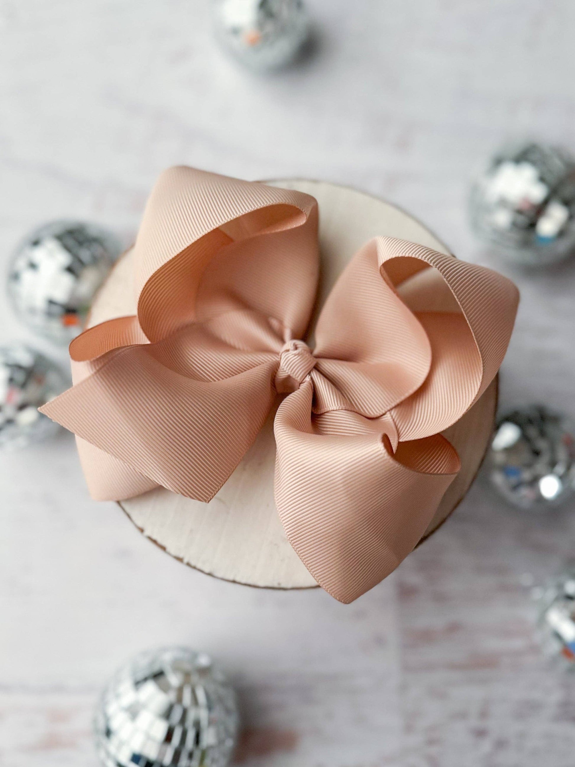 Large oatmeal colored  bow on a white surface with decorative silver balls in the background