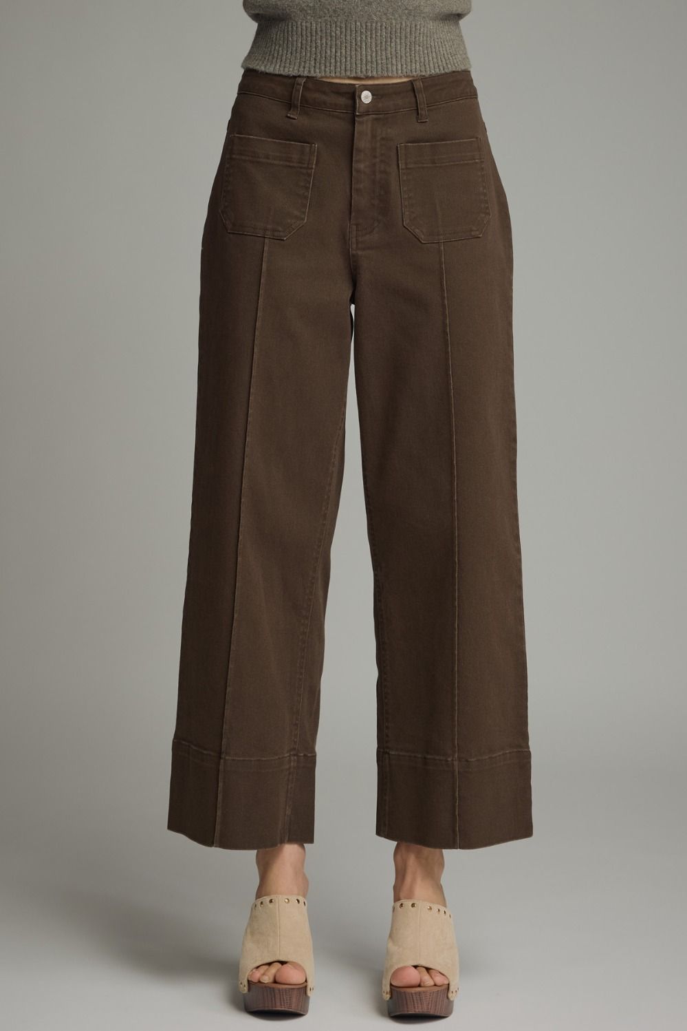 Brown wide-leg pants worn with a gray sweater on a plain background