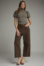 Woman wearing a gray turtleneck and brown pants against a plain background