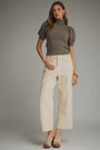 Woman wearing a brown turtleneck top and beige pants against a gray background