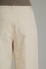 Close-up back view of a person wearing light beige wide-leg trousers with a ribbed taupe knit top visible at the waistband, against a plain light gray studio background.