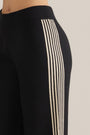 Black pants detail with narrow cream vertical stripes along one leg seam.