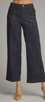 A model wearing dark indigo wide-leg cropped denim pants with beige pointed-toe flats, shown from the waist down against a neutral gray studio background.