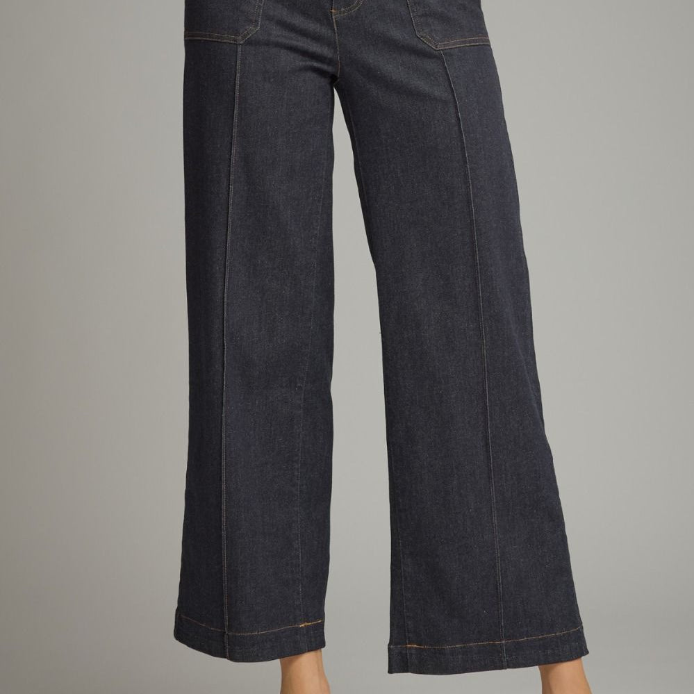 A model wearing dark indigo wide-leg cropped denim pants with beige pointed-toe flats, shown from the waist down against a neutral gray studio background.
