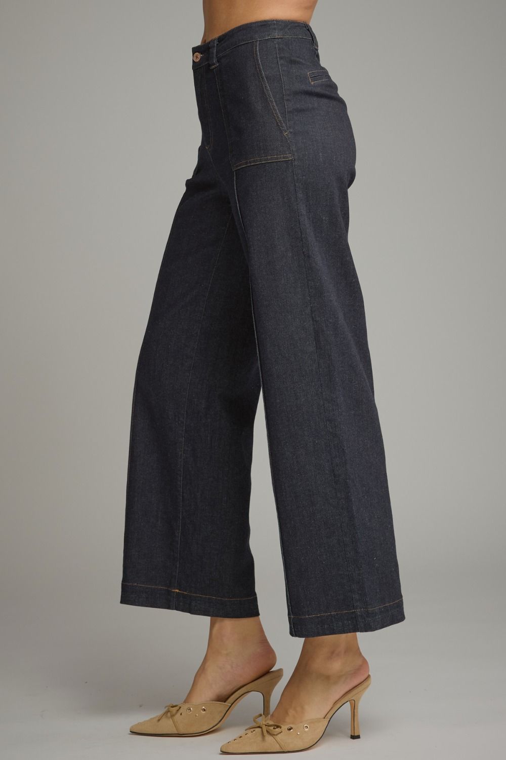 A person wearing dark indigo wide-leg cropped jeans with tan heeled mule sandals, shown from the waist down against a plain light gray studio background.