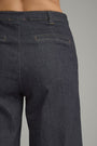 Close-up back view of a person wearing dark indigo denim jeans, showing the waistband, belt loops, back pockets, and fabric texture against a plain gray background.