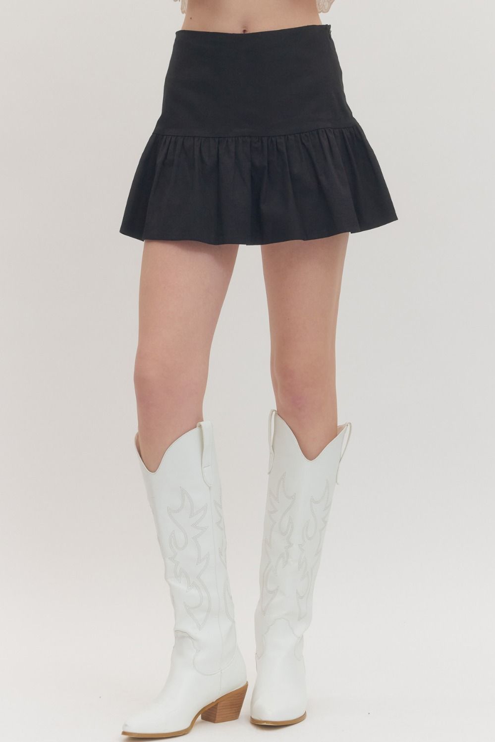 Person wearing a black skirt and white cowboy boots on a plain background