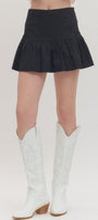 Person wearing a black skirt and white cowboy boots on a plain background