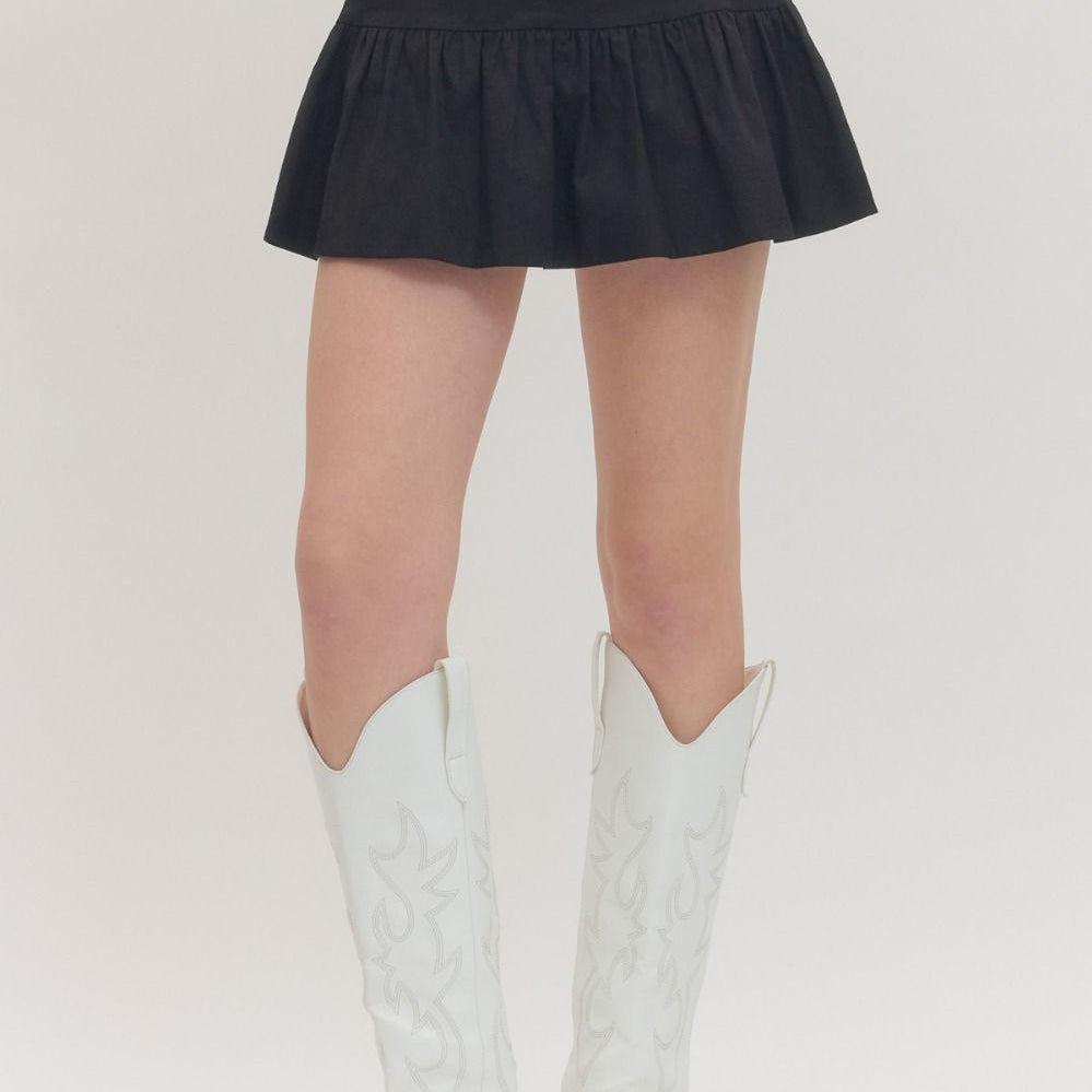 Person wearing a black skirt and white cowboy boots on a plain background