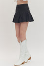 Person wearing a black skirt and white knee-high boots on a light gray background
