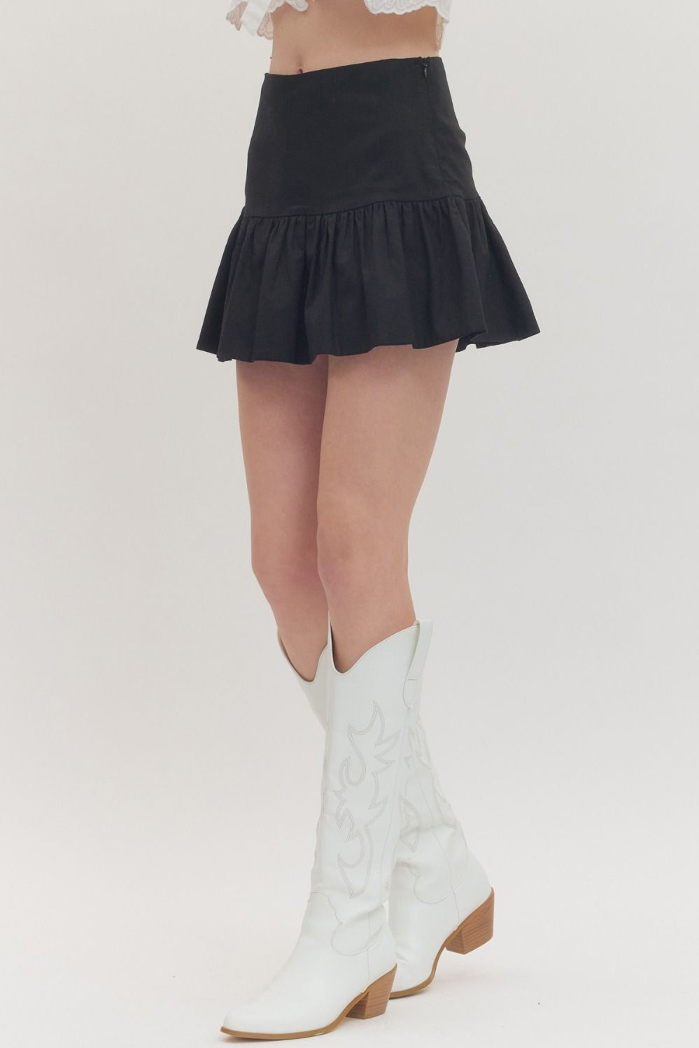 Person wearing a black skirt and white knee-high boots on a light gray background
