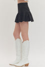 Person wearing a black skirt and white knee-high boots on a plain background