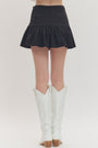 Black skirt worn by a person with white knee-high boots on a plain background