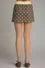 Person wearing a brown polka dot skirt on a gray background