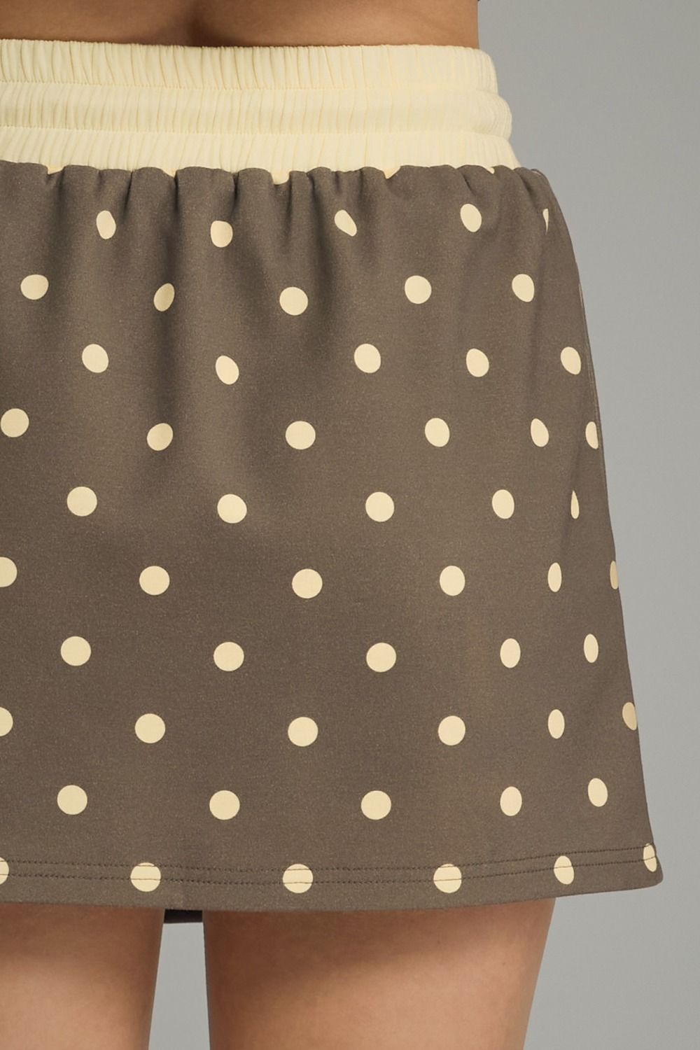 Brown polka dot skirt with beige waistband on a gray background