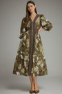A woman models a long-sleeved midi dress with a green, brown, and beige floral print, featuring a dark brown vertical stripe down the front and a matching dark brown waist tie, set against a solid gray studio background.