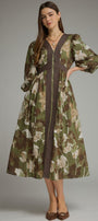 A woman models a long-sleeved midi dress with a green, brown, and beige floral print, featuring a dark brown vertical stripe down the front and a matching dark brown waist tie, set against a solid gray studio background.