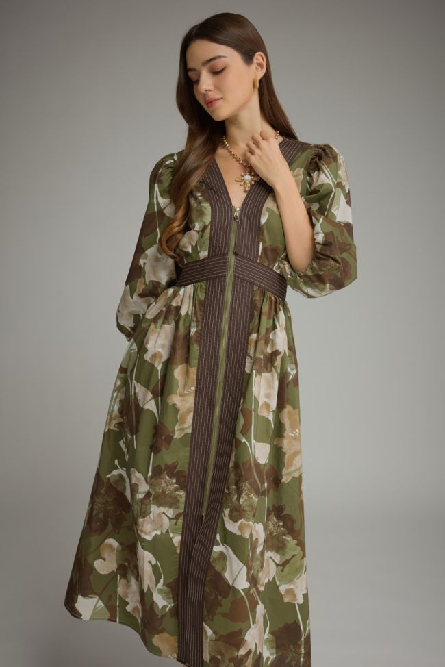 A woman modeling a long-sleeved maxi dress with a green, brown, and beige floral camouflage pattern and dark brown vertical pinstripe details on the front and waist.