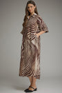 A woman modeling a brown and beige zebra-print midi shirt dress with three-quarter sleeves and a collar, paired with black flat shoes, against a neutral gray studio background.