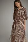 A woman wearing a brown and beige zebra-print midi shirt dress, standing against a neutral gray studio background.