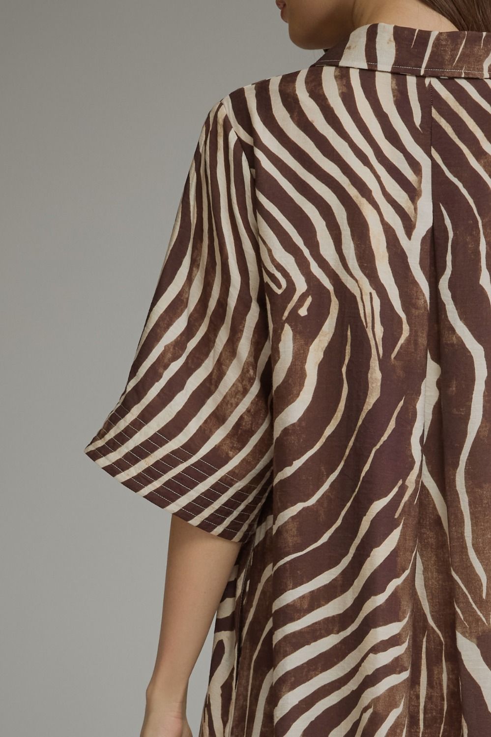 A close-up of a person wearing a brown and cream zebra-print shirt, showing the side and back view against a neutral gray background.