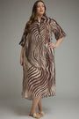 A woman modeling a brown and beige zebra-print midi shirt dress with short sleeves, a button-up front, and a relaxed fit, photographed against a neutral gray studio background.
