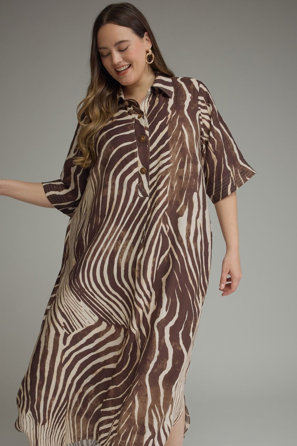 A woman modeling a brown and beige zebra-print shirt dress against a solid gray studio background.