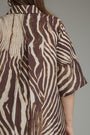 A close-up of a person wearing a short-sleeve button-up shirt with a brown and beige zebra-like abstract pattern, shown from the back against a plain gray background.
