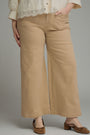 A person wearing beige wide-leg cropped pants with a cream lace-trim blouse and brown mule flats, shown from the chest down against a light gray studio background.