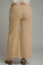 A person shown from the back wearing beige wide-leg cropped pants, a white lace-trim top, and brown heeled sandals against a plain gray studio background.