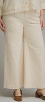 A person wearing cream wide-leg cropped pants with a matching cream lace-trim blouse and brown mule heels, photographed against a plain light gray studio background.