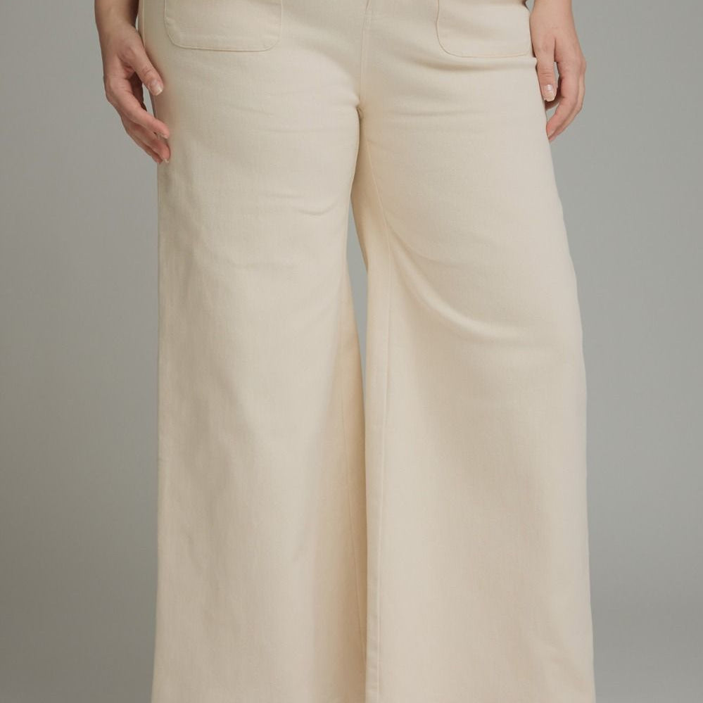 A person wearing cream wide-leg cropped pants with a matching cream lace-trim blouse and brown mule heels, photographed against a plain light gray studio background.
