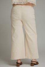 A person shown from the back wearing off-white cropped wide-leg pants and brown flat shoes against a plain light gray studio background.