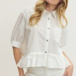 Woman wearing a white blouse with ruffled details and white pants against a plain background