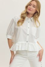 Woman wearing a white blouse with ruffled details and white pants against a plain background