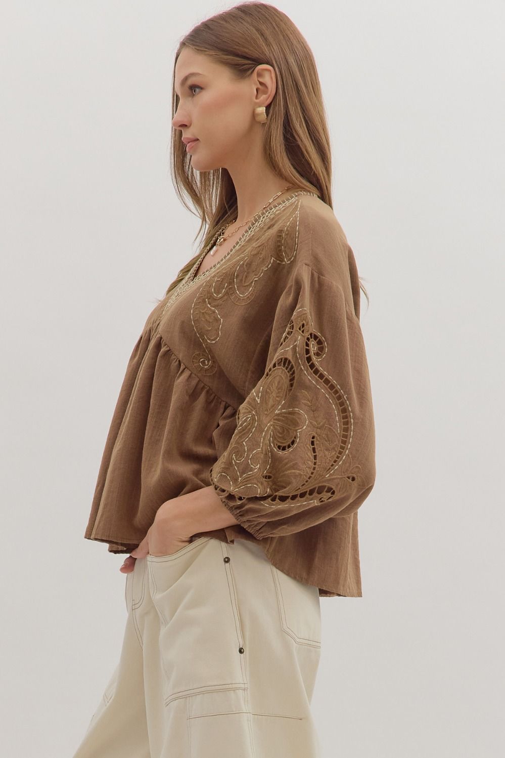 girl wearing a long sleeve brown top with light and dark brown thread details.