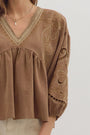 girl wearing a long sleeve brown top with light and dark brown thread details.