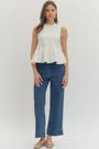 Woman wearing a white sleeveless peplum top and blue jeans on a white background