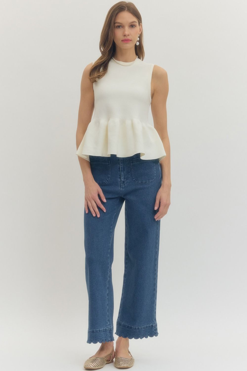 Woman wearing a white sleeveless peplum top and blue jeans on a white background