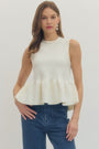 Woman wearing a white peplum top and blue jeans on a plain background