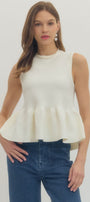 Woman wearing a white peplum top and blue jeans on a plain background