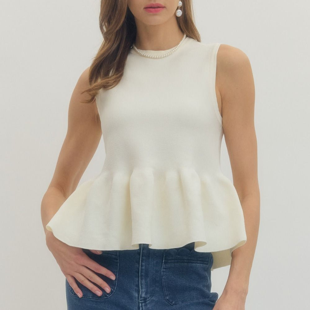 Woman wearing a white peplum top and blue jeans on a plain background