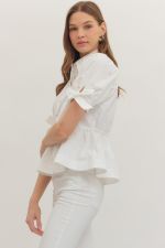 Woman wearing a white blouse and pants against a plain background